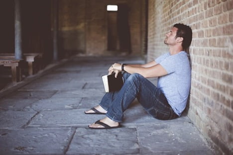 Law of attraction man sitting leaning against the wall with book in hand