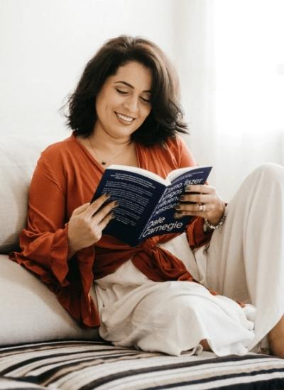 Dark Haired woman reading a book while sitting on the bed