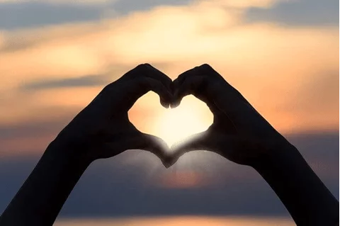 hands make a heart-shaped silhouette at sunset